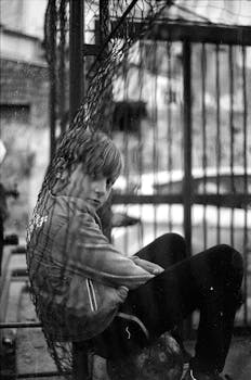 Black and white photo of a child sitting behind a wire cage, looking thoughtful.