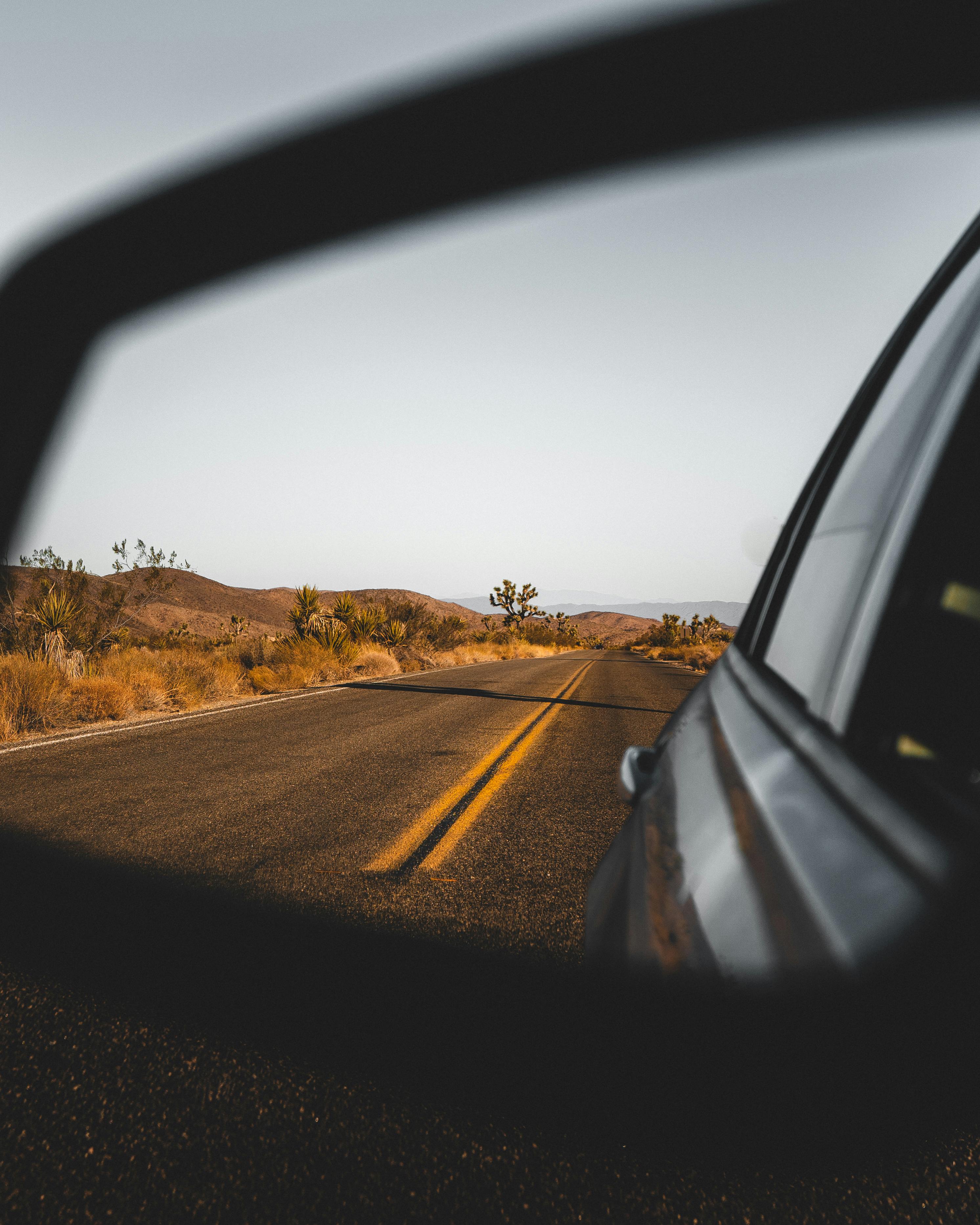 A desert highway seen through a car's side mirror under a clear sky.