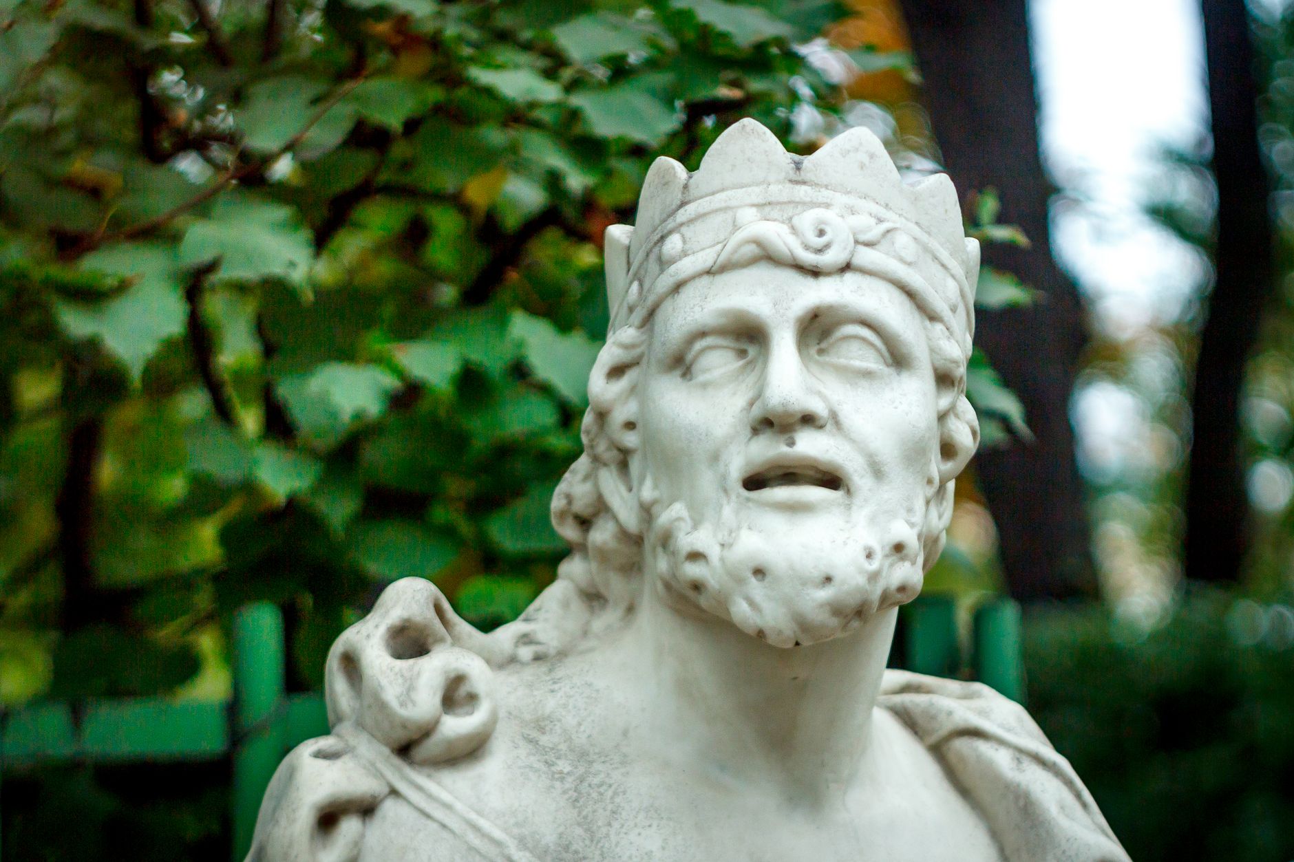 A close-up of a marble statue depicting an ancient king amidst lush greenery.