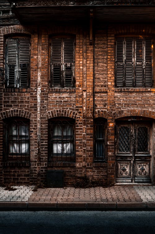 Free Aged brick house exterior with arched windows near tiled pavement and road in city Stock Photo