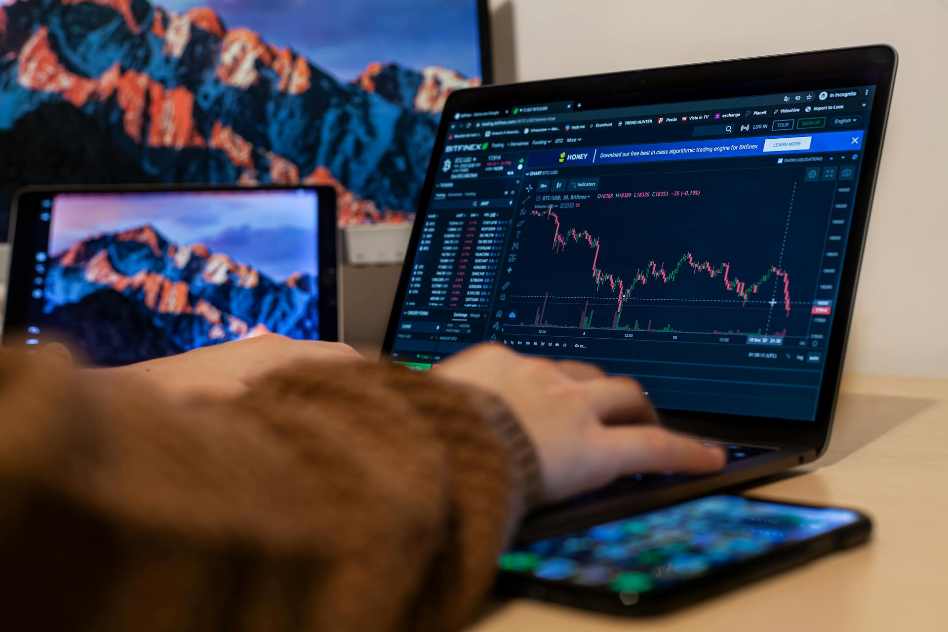 Close-up of hands typing on a laptop with stock charts displayed, analyzing financial data.