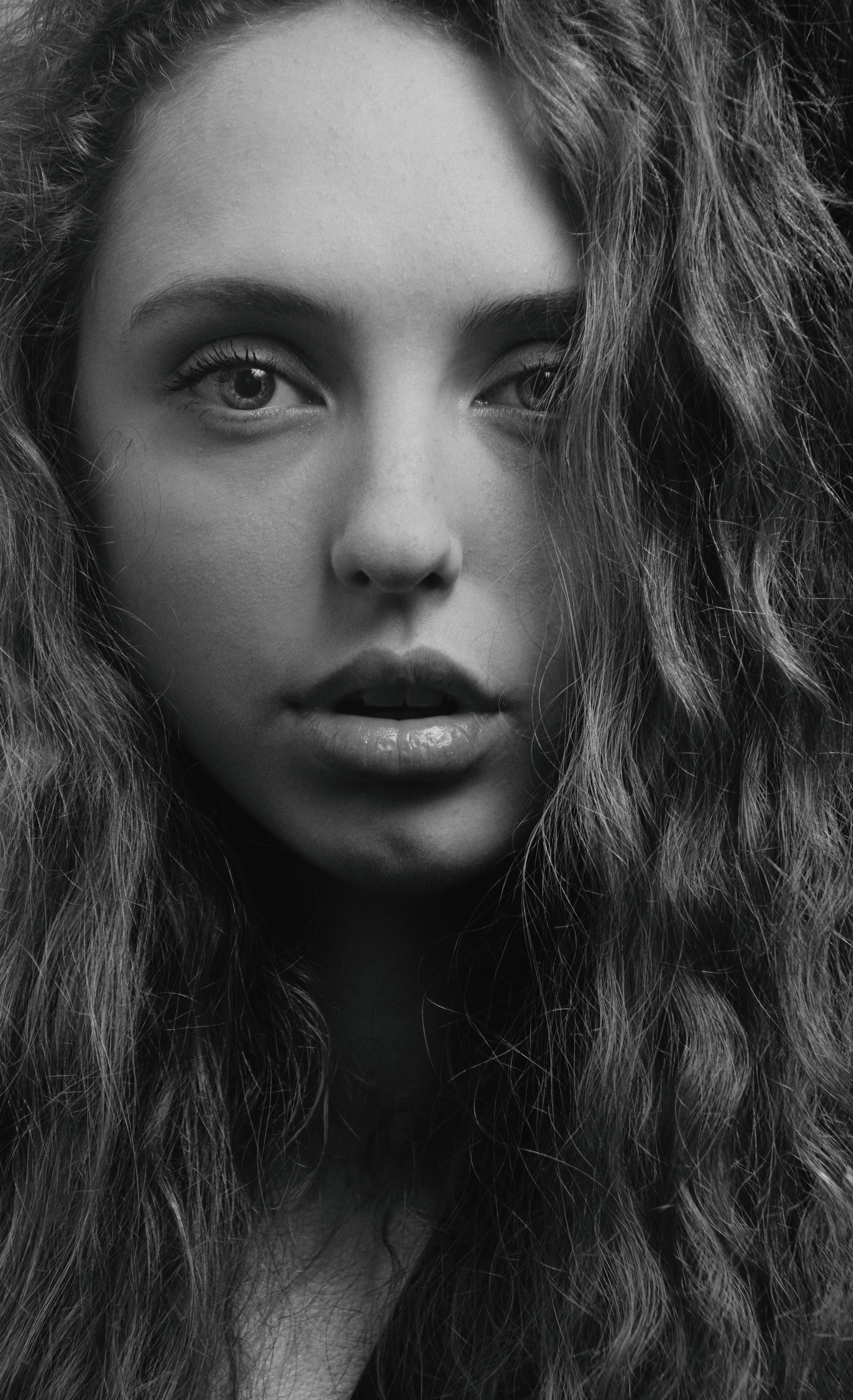 Captivating grayscale headshot of a woman with curly hair looking at the camera.