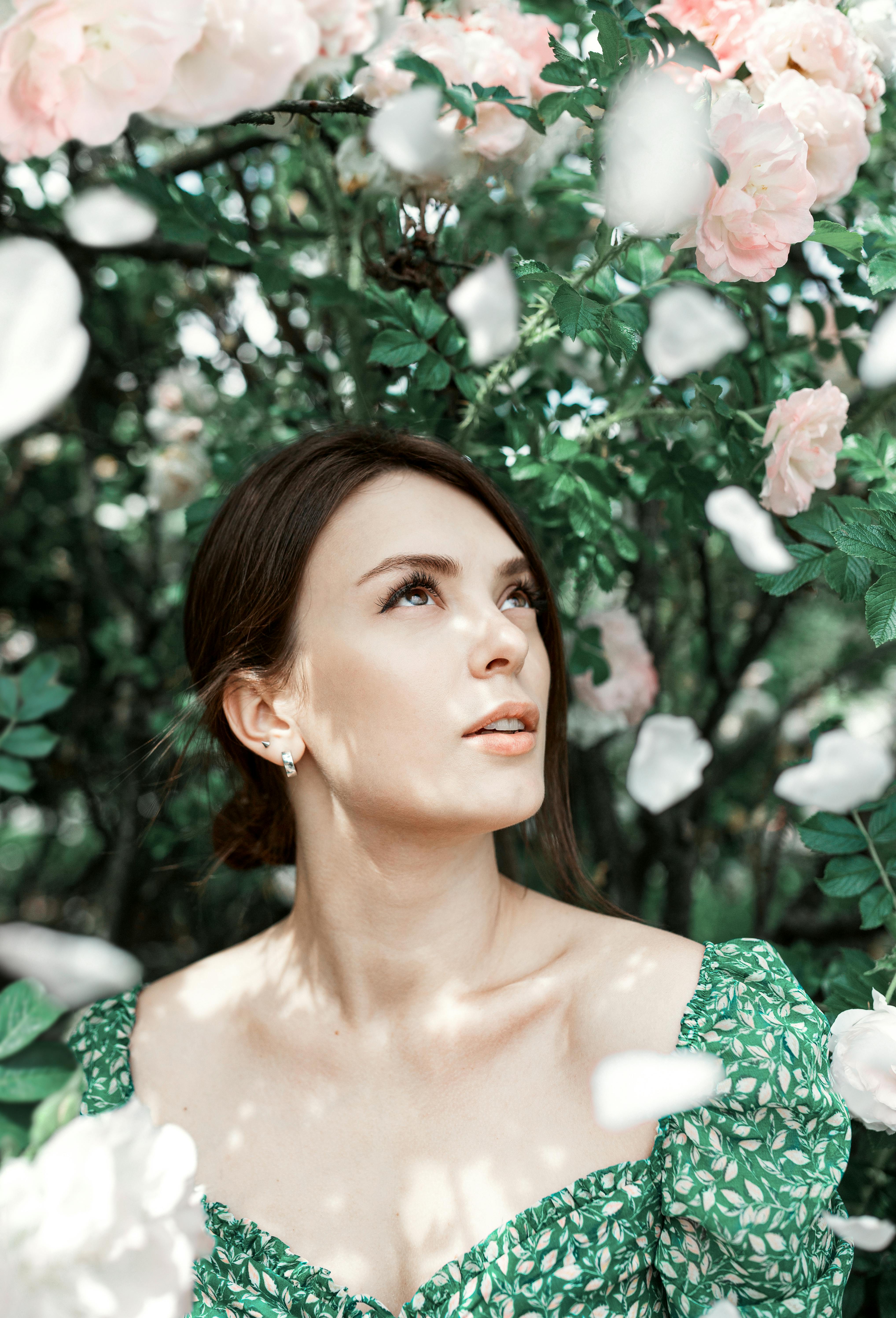Portrait of a woman in a green dress gazing up among pink blossoms.