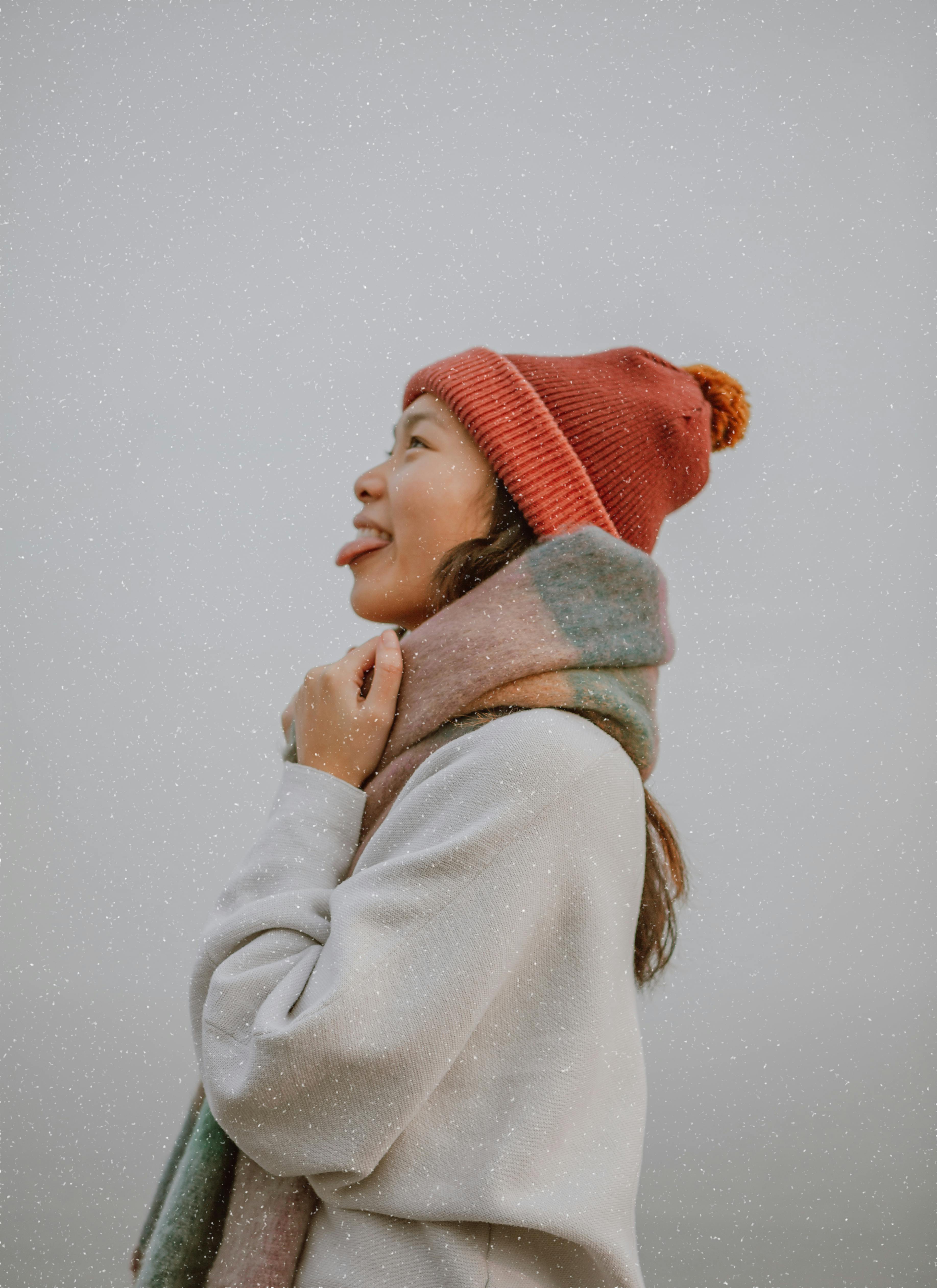 Side profile of a young woman in warm clothes, smiling and enjoying a snowy day in Toronto.