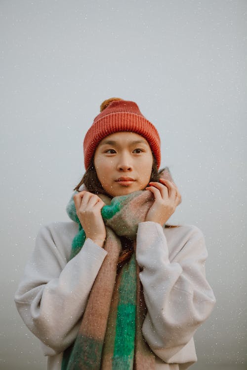 Dreamy Asian woman in warm clothes on gray background · Free Stock Photo