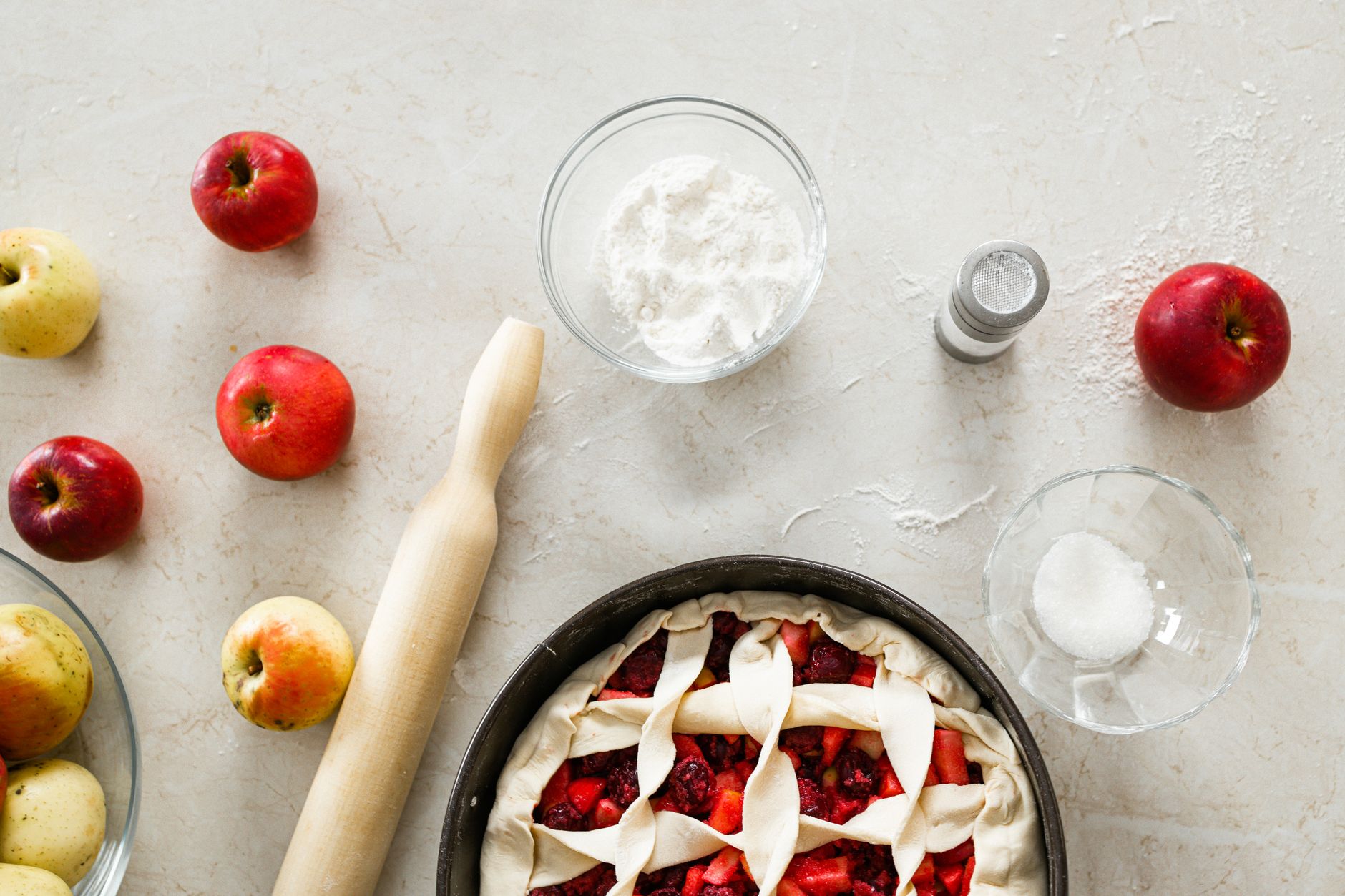 Top view of apple pie preparation with raw ingredients and rolling pin on a countertop.