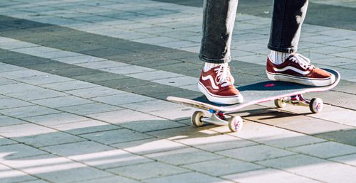 Free Skateboarder wearing red sneakers rides on a tiled surface in daylight, showcasing street style. Stock Photo