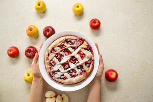 Free Hands holding a freshly baked fruit pie surrounded by apples on a light surface. Perfect for autumn themes. Stock Photo