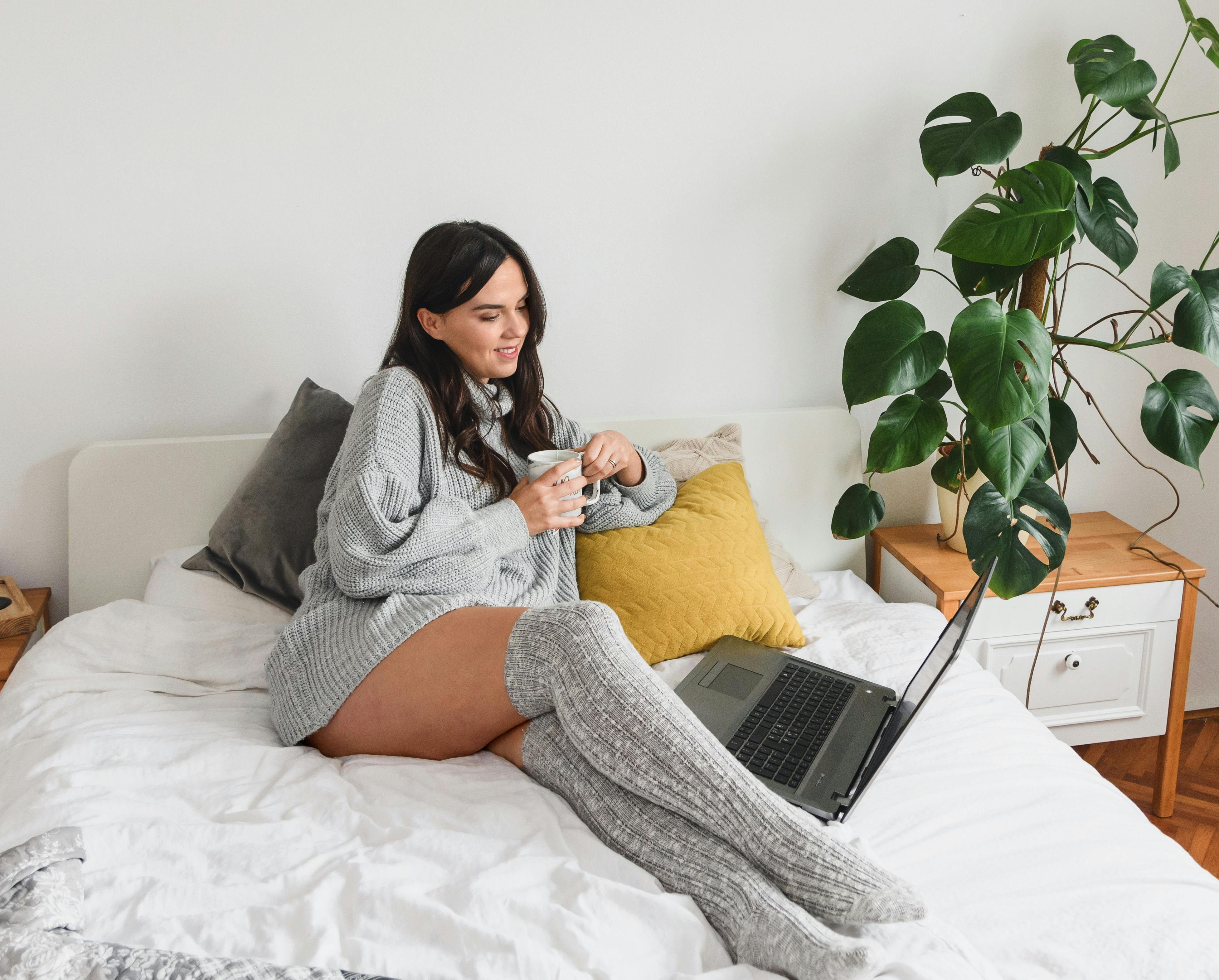 Content woman with hot beverage watching movie on laptop indoors · Free Stock Photo