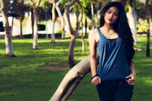 一位身着蓝色上衣的优雅亚洲女子，在阳光明媚的公园背景下优雅地摆出姿势