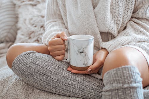 Crop woman with mug of hot drink on bed
