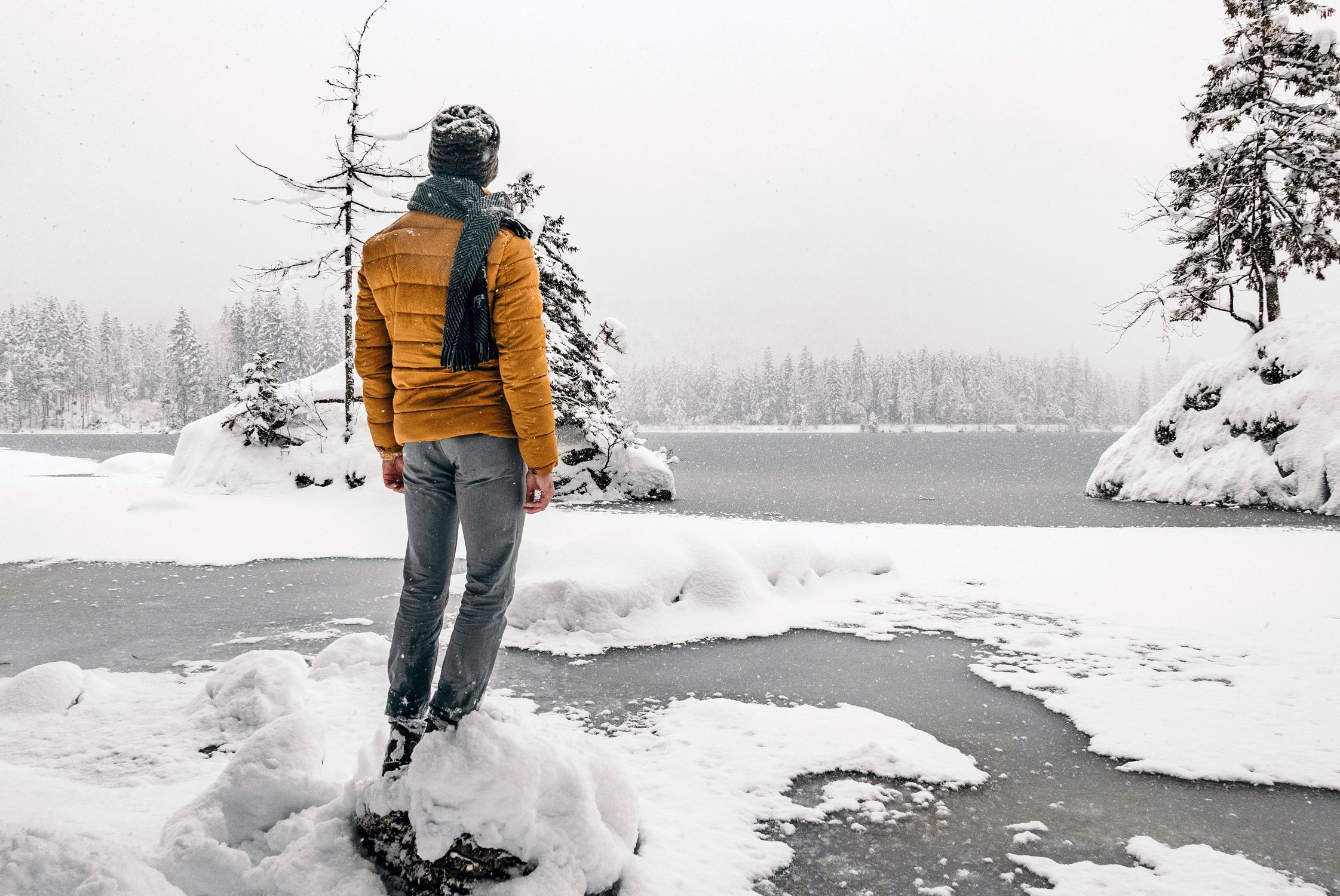 Man standing on a snowy shore gazing at a frozen lake in a serene winter landscape