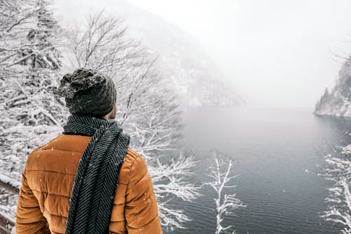 Unrecognizable traveler contemplating foggy sea and snowy mountains in wintertime