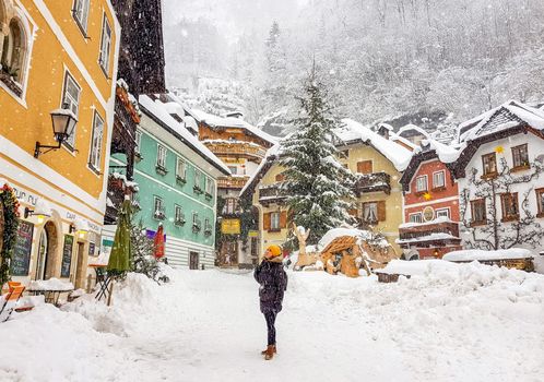 Side view of female tourist looking up on pathway against bright dwelling houses and trees during snowfall