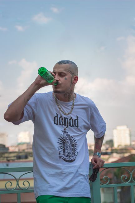 Tattooed man drinking beer outdoors in city setting, capturing modern urban lifestyle.