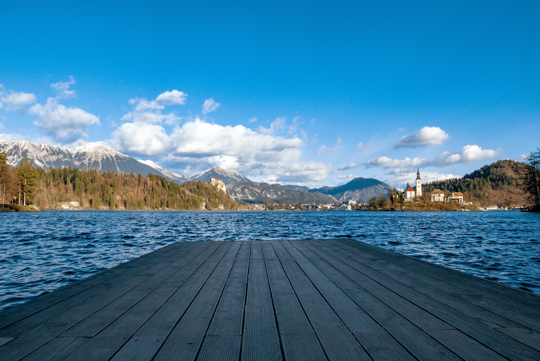 Photo by Marko Klaric Wooden pier at Lake Bled with the island church and forested mountains under a bright sky