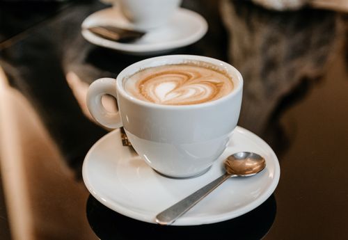 Free White cup of freshly brewed hot latte placed on saucer and served on table in cafeteria Stock Photo