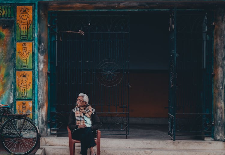 An Elderly Man Sitting On A Chair Outside