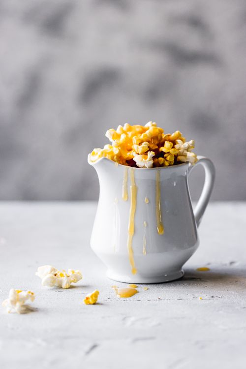 Free Delicious caramel popcorn spilling from a white jug, artistic food display. Stock Photo