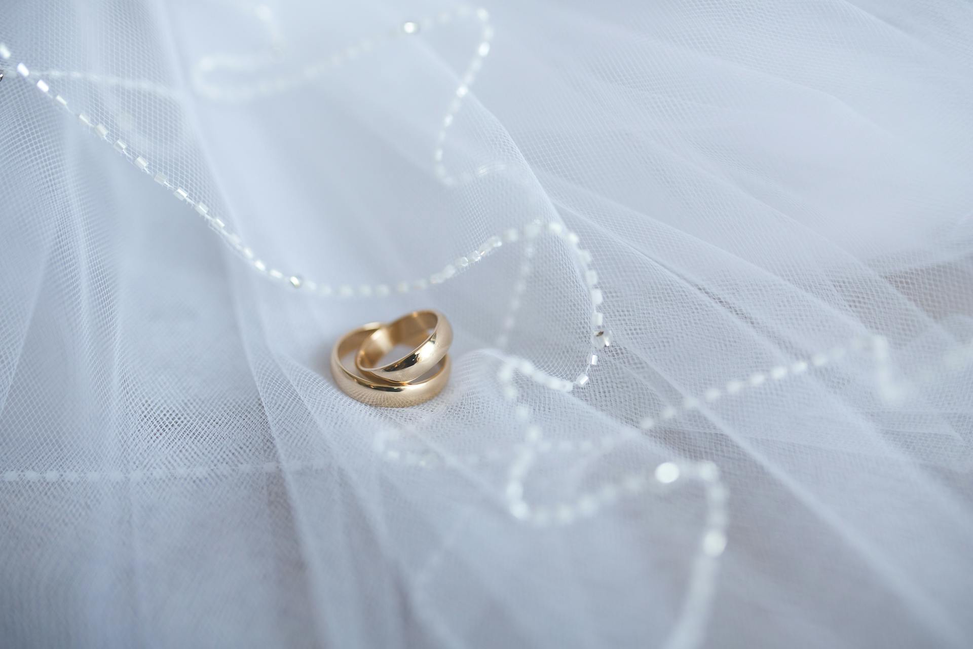 Beautiful gold wedding rings resting on soft white tulle with delicate beaded details, symbolizing love and commitment.
