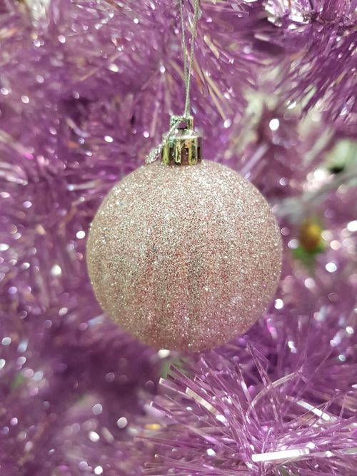 Free Close-up of a sparkling Christmas bauble hanging on a vibrant pink tinsel tree. Stock Photo