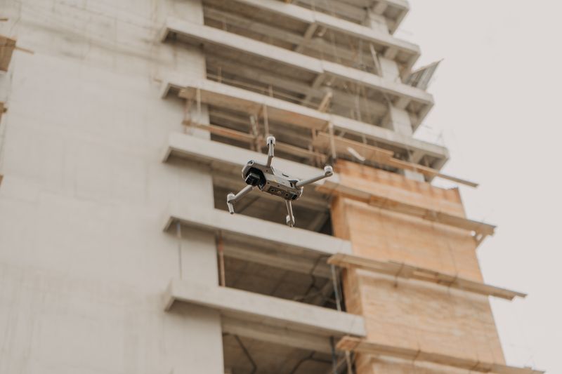 A quadcopter drone hovers near an unfinished high-rise construction site under overcast skies