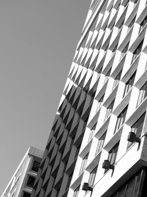 From below black and white of contemporary geometric building with glass windows under sky