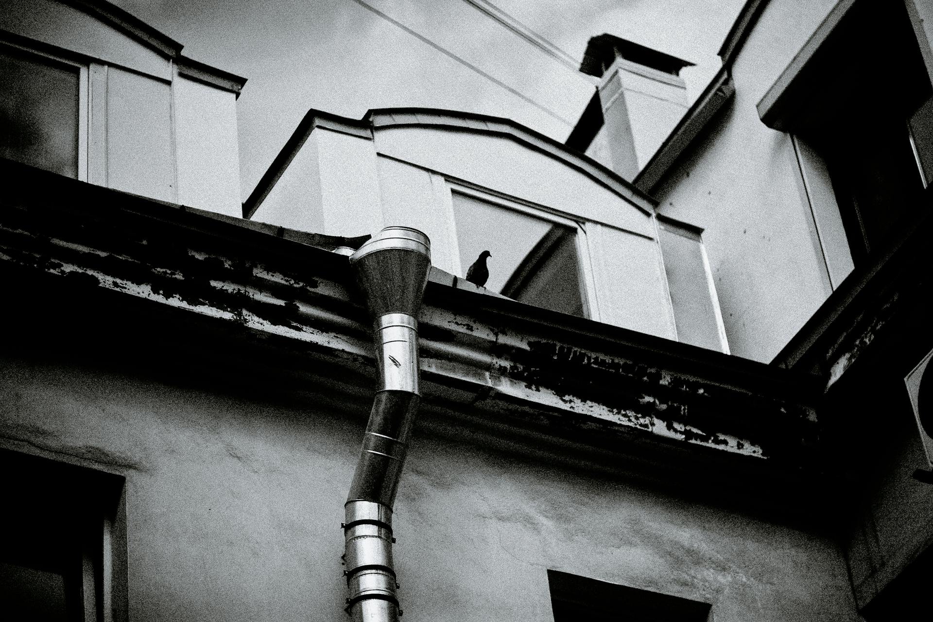 From below black and white of aged building exterior with drain pipe under cloudy sky in city