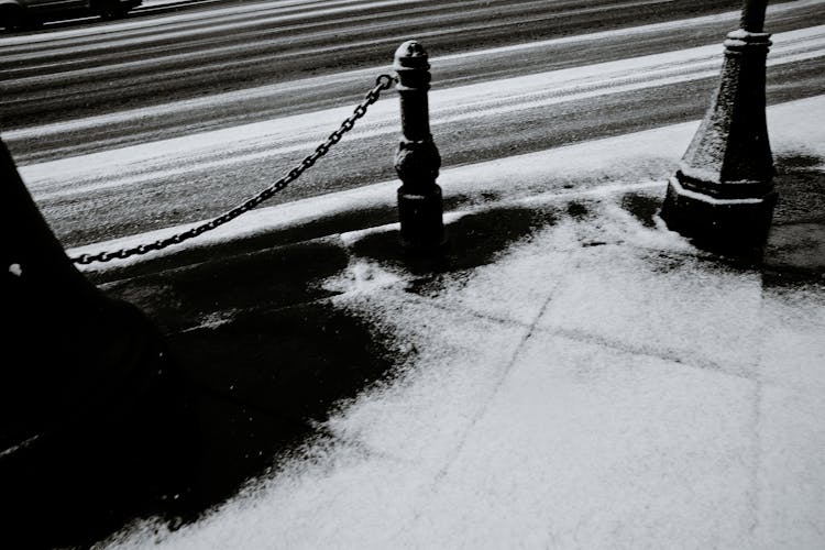 Fence With Chain Against Snowy Pavement In Town