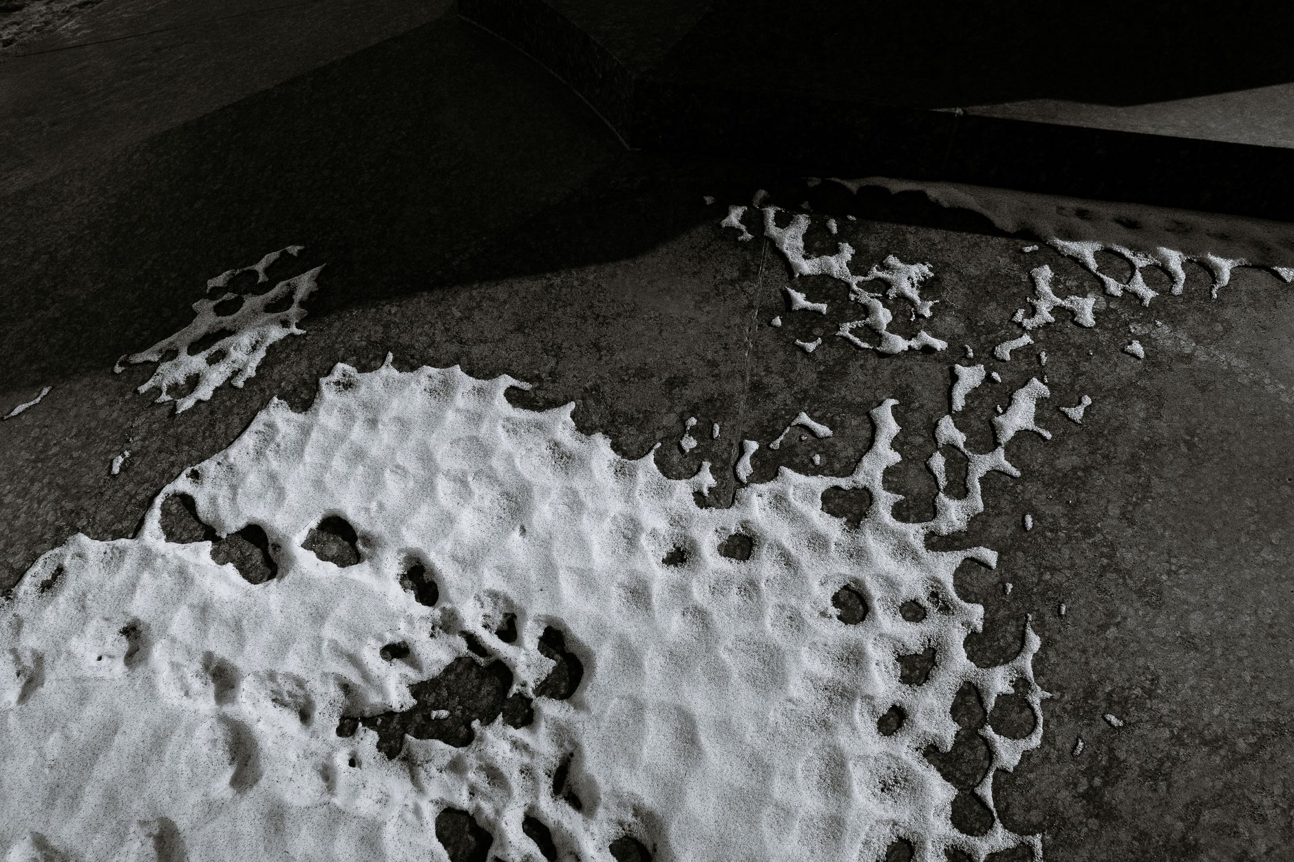 From above black and white of snow on asphalt walkway in city in cold weather