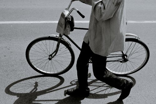 Free Side view of black and white crop anonymous person in stylish outfit walking on asphalt road with bicycle on sunny day Stock Photo