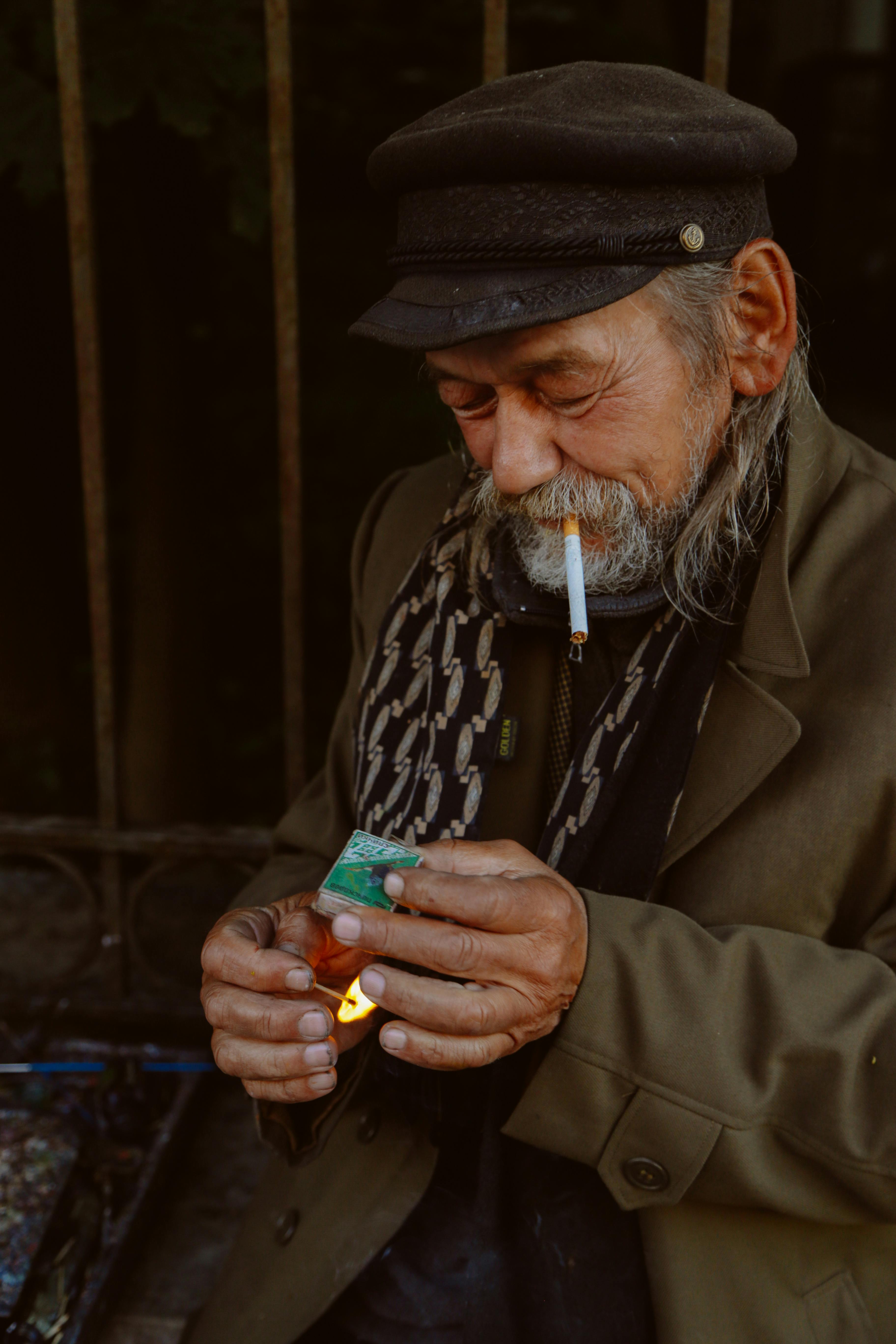 elderly ethnic man lighting match while smoking cigarette on street