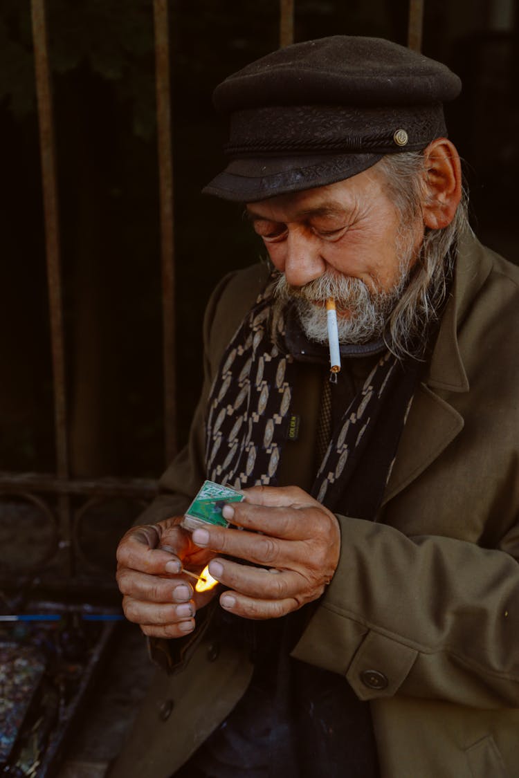 Elderly Ethnic Man Lighting Match While Smoking Cigarette On Street