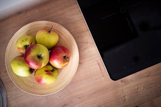 Top view of fresh apples in a wooden bowl on a kitchen counter next to a stovetop.