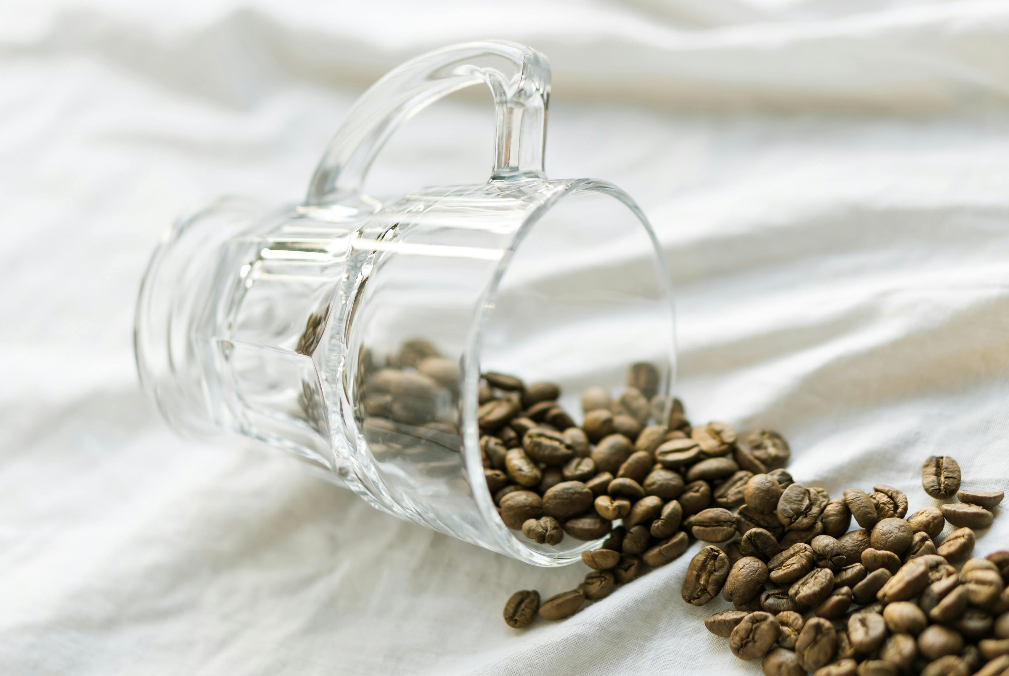 Close-up of coffee beans spilling from a glass mug onto white fabric, creating a calming and minimalist aesthetic.
