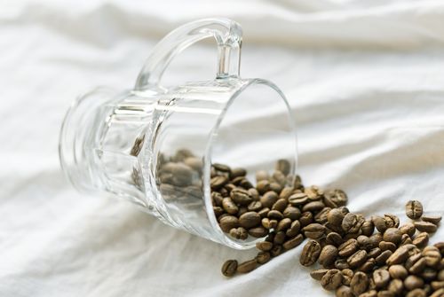 Free Close-up of coffee beans spilling from a glass mug onto white fabric, creating a calming and minimalist aesthetic. Stock Photo