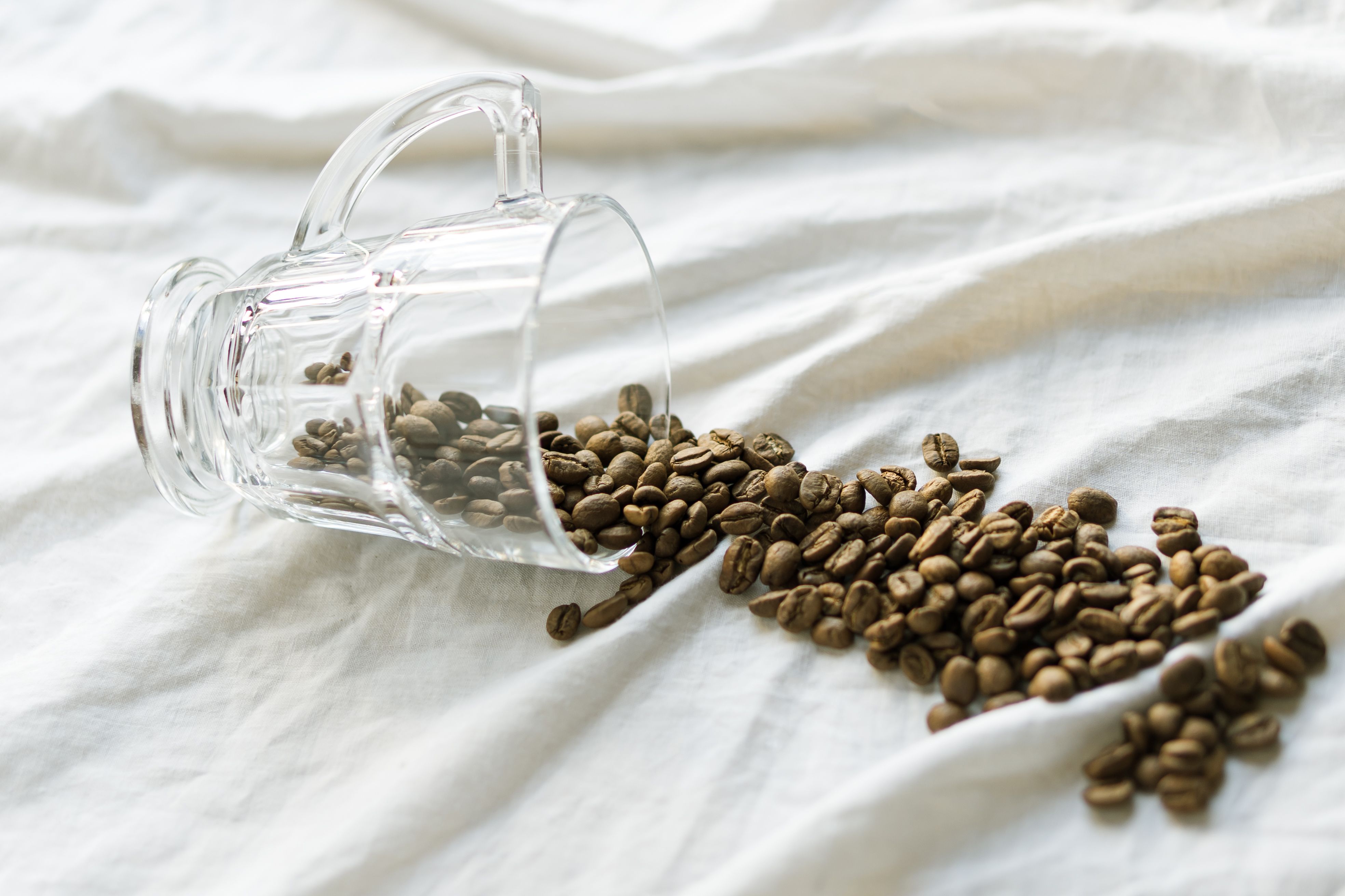 Clear glass mug of coffee beans on white cloth, showcasing minimalism.
