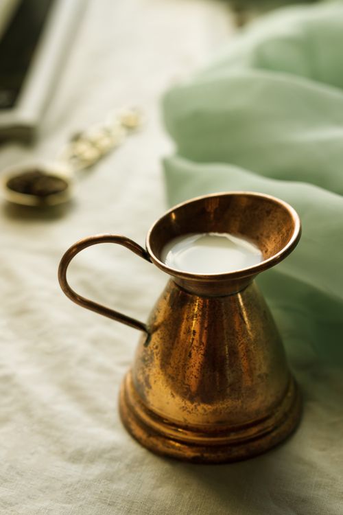 Free Close-up of a vintage brass pitcher filled with milk on a rustic table. Ideal for kitchen and home decor themes. Stock Photo