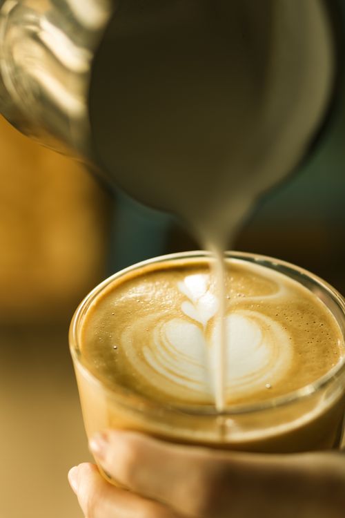 Free Detailed close-up of barista making latte art by pouring milk into coffee. Perfect for cafe or coffee shop themes. Stock Photo