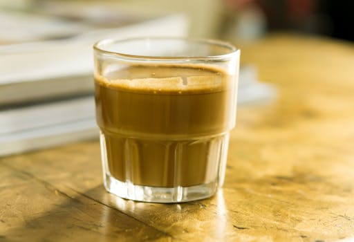 A richly colored espresso shot in a clear glass sitting on a wooden table indoors.