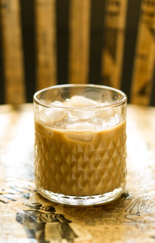 Free Close-up shot of iced coffee in a textured glass on a vintage newspaper-covered table. Stock Photo