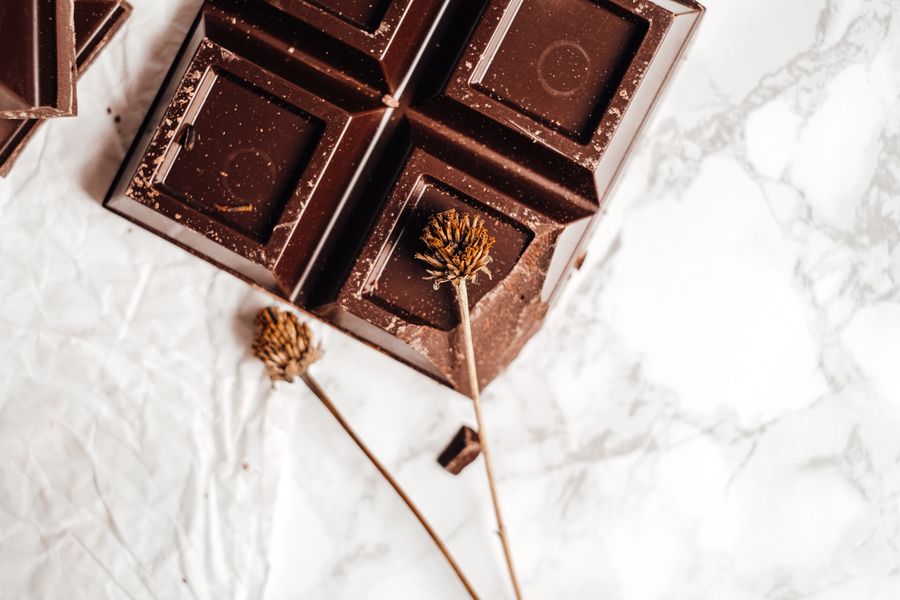 Close-up of a dark chocolate bar on marble with dried flowers, showcasing elegance in food photography.
