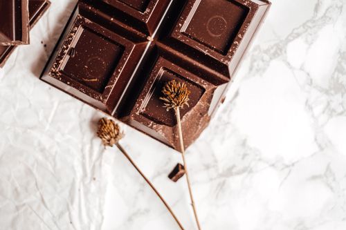 Free Close-up of a dark chocolate bar on marble with dried flowers, showcasing elegance in food photography. Stock Photo