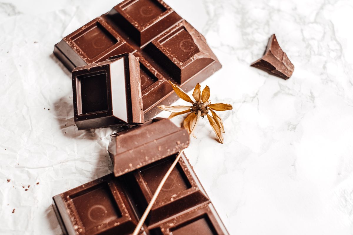 A close-up of a chocolate bar on a white background with a dried flower for decoration.
