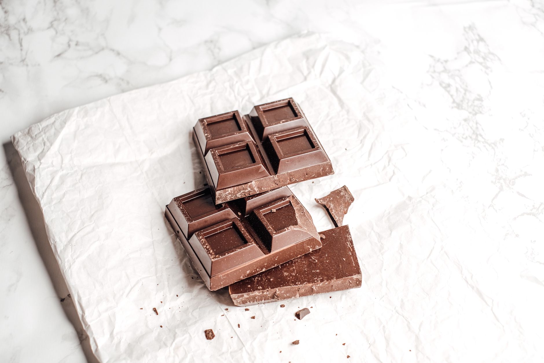 Close-up of dark chocolate bar on crumpled white paper, showcasing texture.