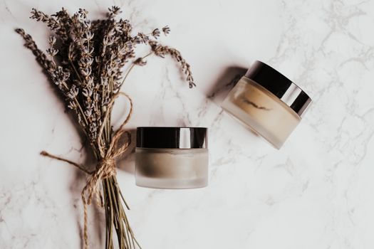 Skincare jars and lavender arranged on a marble surface, perfect for beauty and wellness themes.