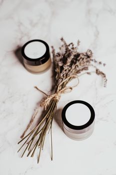 Stylish flat lay of skincare jars with dried lavender on a marble surface.