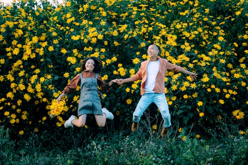 Joyful Asian couple jumping near blooming flowers