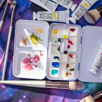 A colorful array of watercolor paints, brushes, and tubes on a creative surface, perfect for artistic inspiration.（イメージ）