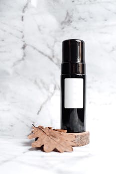 Minimalist skincare bottle with autumn leaf on marble, perfect for beauty product mockups.